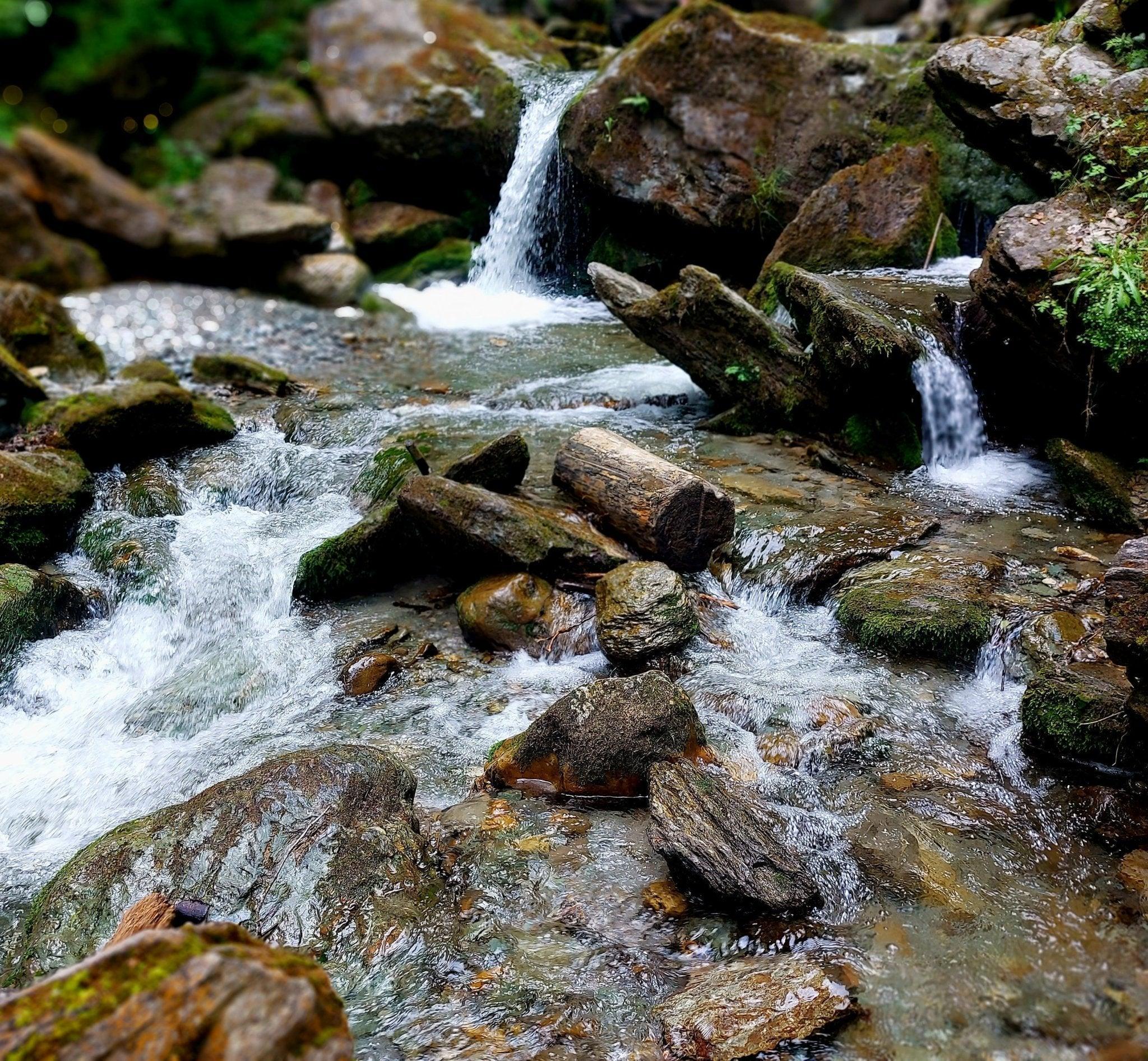 Klare Bergbach mit moosbedeckten Steinen und kleinen Wasserfällen