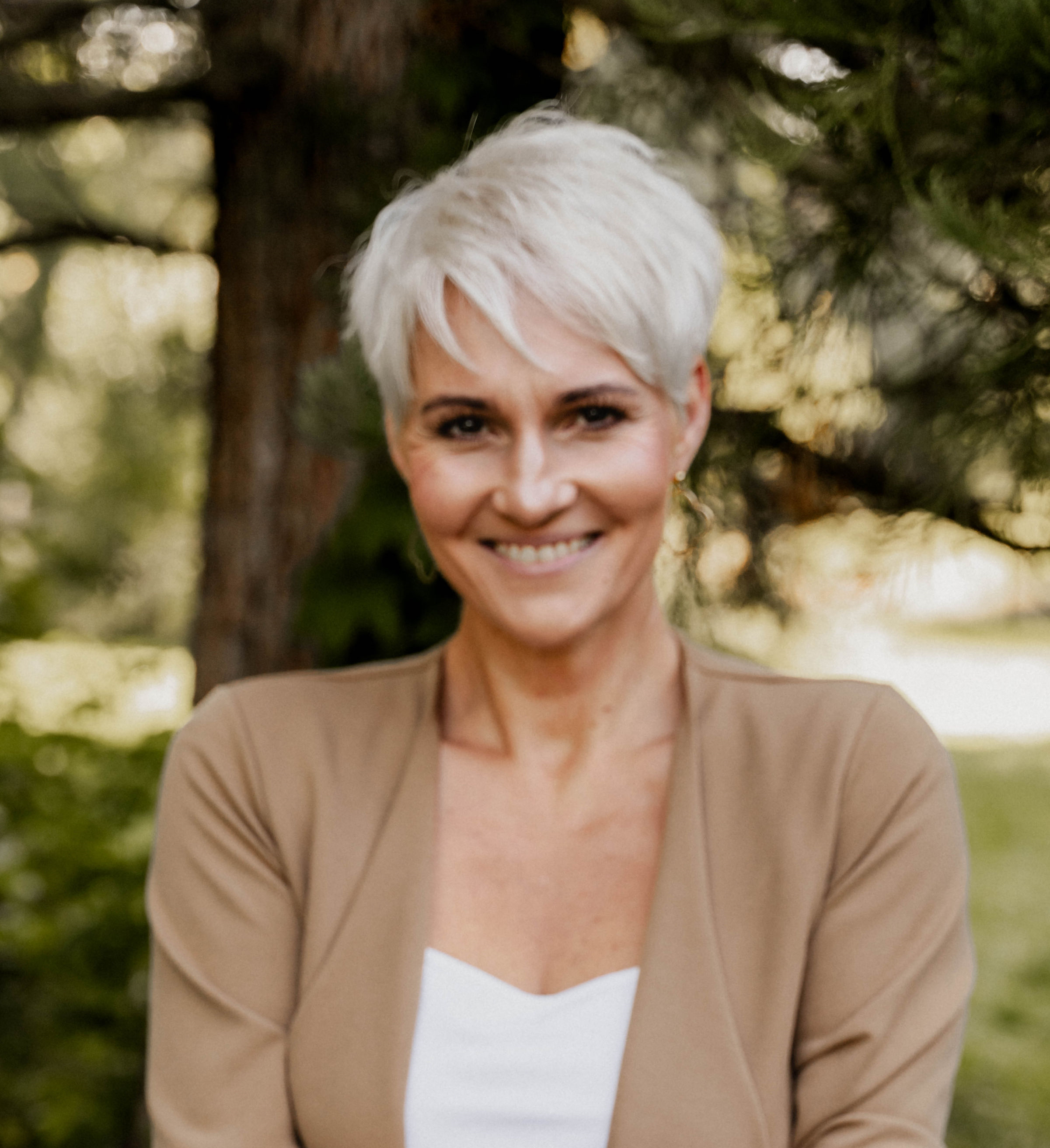Frau mit kurzen blonden Haaren im Freien, lächelnd, natürlicher Hintergrund